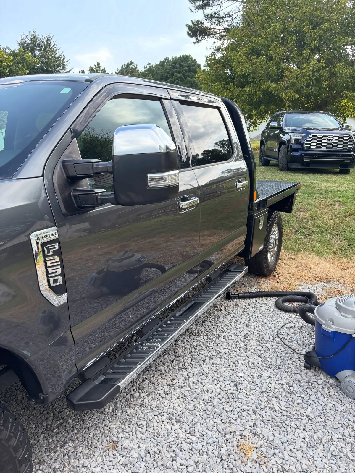 Dark grey Ford F-250 flatbed being detailed on site with a shop vacuum and hoses alongside